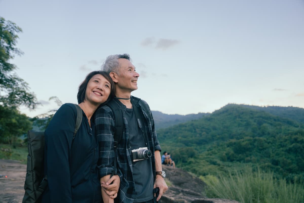 Retired couple smiling together while hiking, with a mountain view behind them